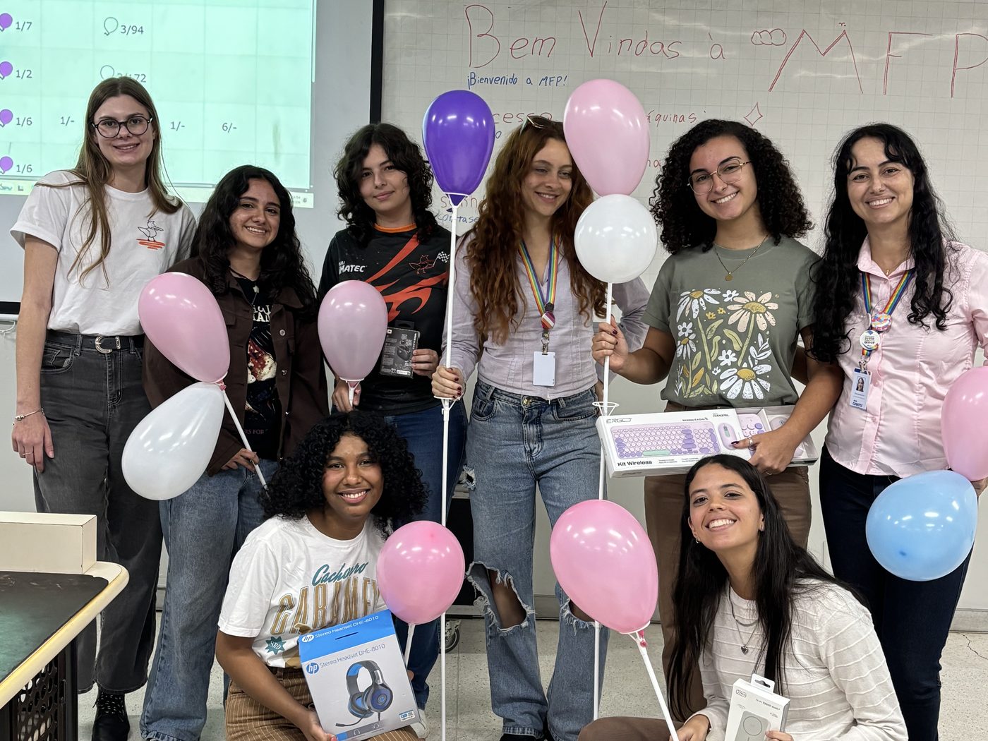 Participantes da Maratona Feminina de Programação reunidas na sala, com balões e o quadro escrito 'Bem vindas à MFP'