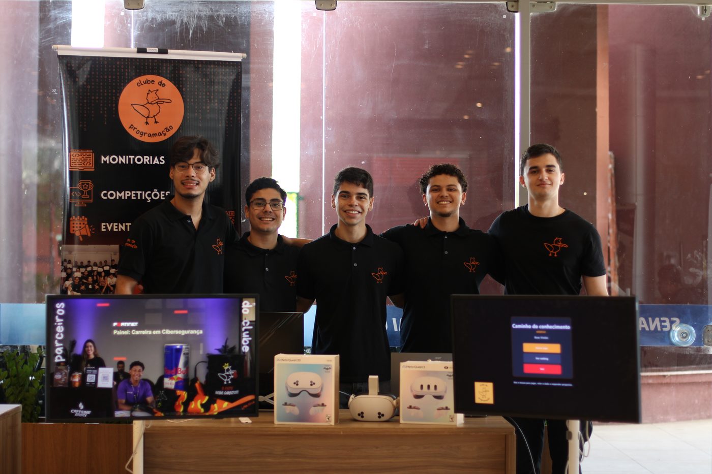 Membros do Clube de Programação no estande do evento, com o banner do clube ao fundo
