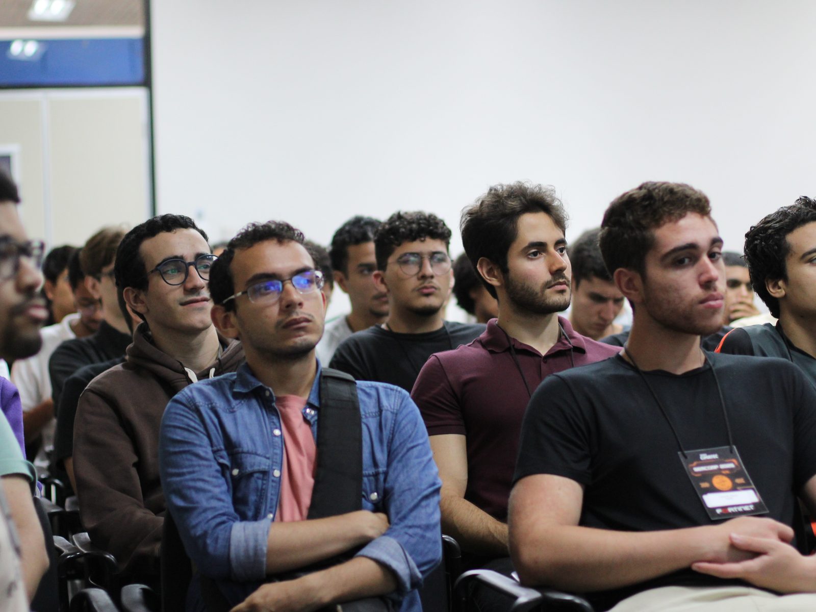 Plateia da SEMCOMP acompanhando uma palestra no auditório da Universidade SENAI CIMATEC, com os crachás do evento no pescoço